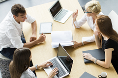 photo of 4 people at a table with laptops having a discussion