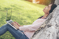 photo of a woman with a laptop sitting against a wall