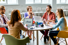 photo of a group of people sitting around a table with laptop computers